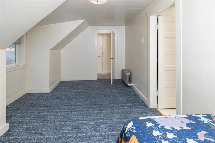 Spacious attic room featuring sloped ceilings, blue patterned carpeting, and white trim