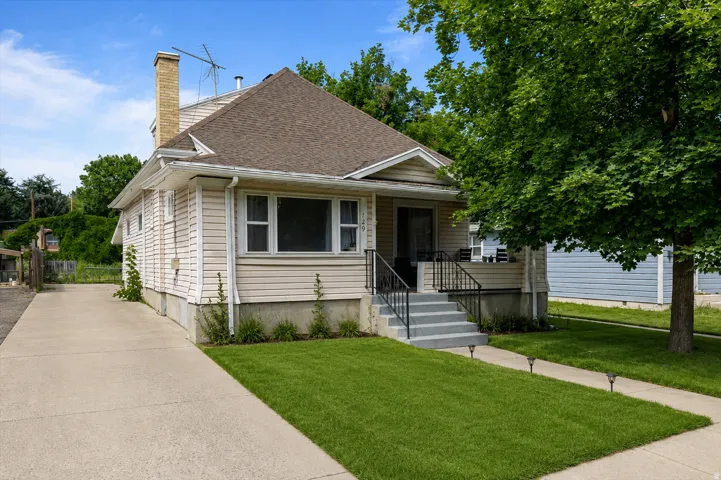 Front entry: Unit #1. Siding exterior featuring a prominent chimney, concrete driveway, front porch with black railing, and a mature tree providing shade
