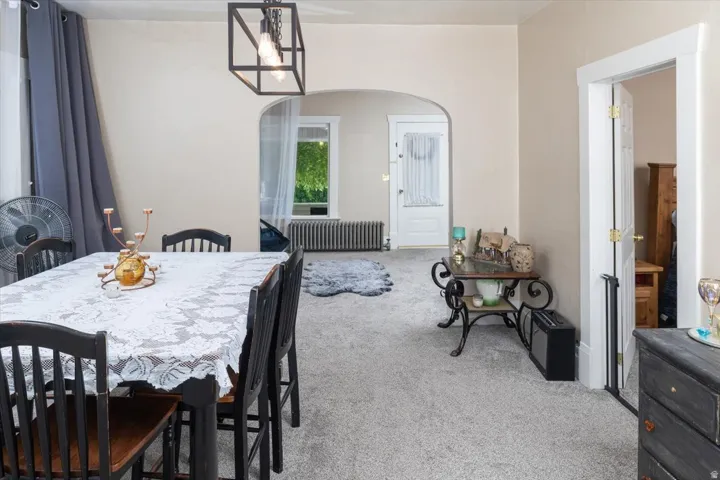 Carpeted dining area featuring a contemporary open-frame chandelier, an arched doorway, and a white interior door with brass hardware