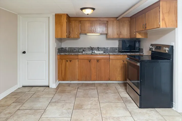 Kitchenette featuring natural wood cabinetry, dark speckled countertops, and a full-size stainless steel and black range