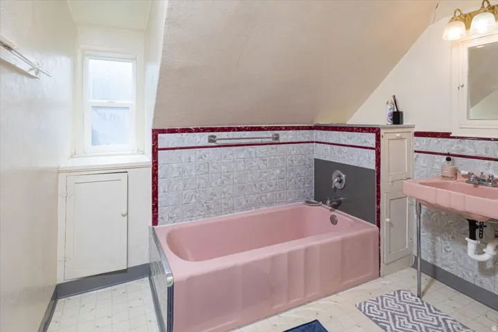 Bathroom featuring a pink tub and sink, white patterned wall tile with red trim, and a built-in storage cabinet