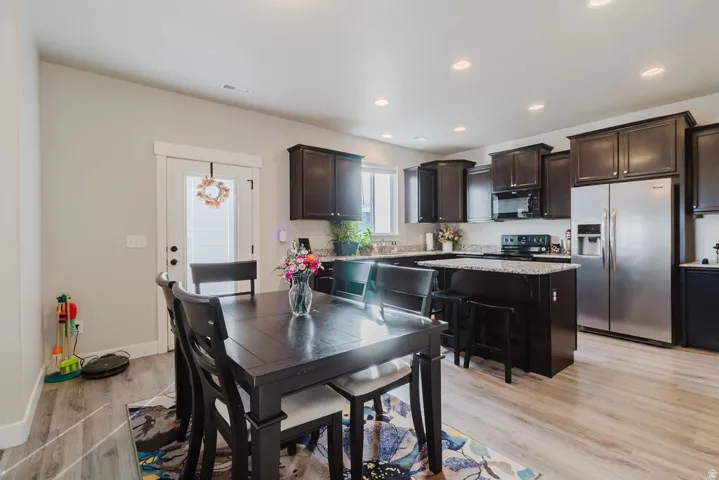 Open-concept kitchen and dining area featuring dark wood cabinetry, stainless steel appliances, granite countertops, and wood-finish flooring