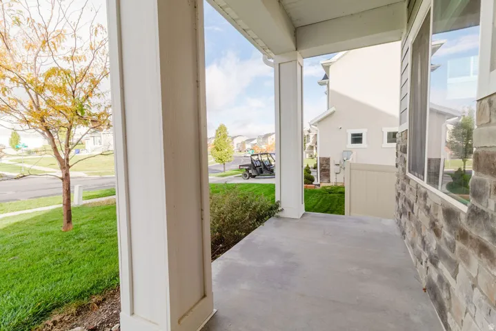 Front porch with a concrete slab, white architectural columns, and stone veneer exterior siding