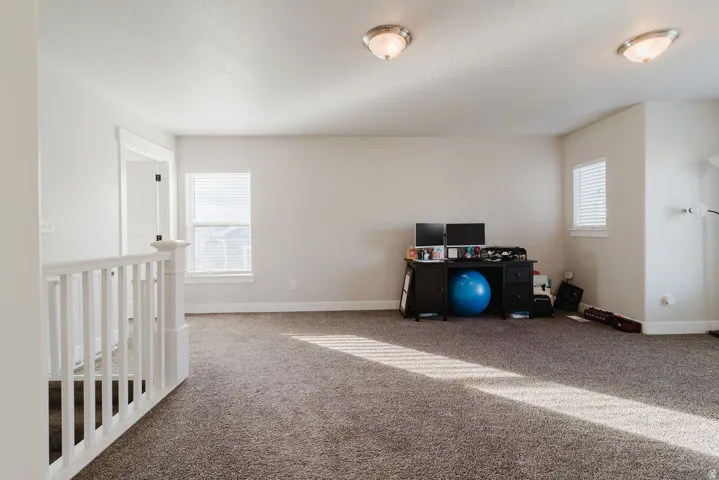 Spacious carpeted room featuring white trim, multiple windows with blinds, and two flush-mount ceiling lights