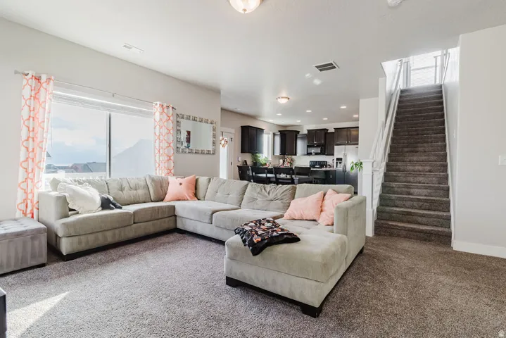 Open-concept living area with abundant natural light, carpeted flooring, and a stairway with white balusters
