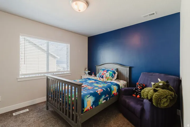 Room featuring a single window with blinds, a dark accent wall, light beige walls, and carpet flooring