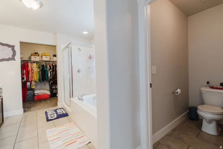 Ceramic tile flooring throughout bathroom with a walk-in shower, built-in bathtub, and an open closet space featuring a built-in hanging rod and shelving