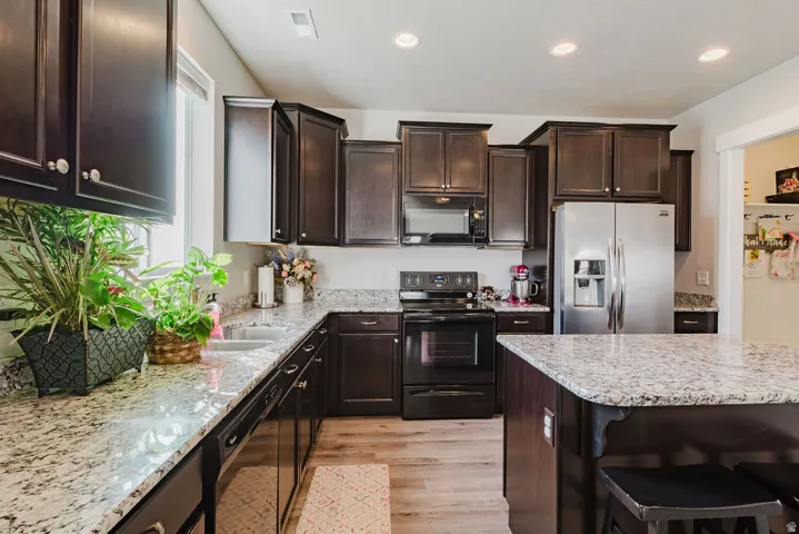 Kitchen featuring dark wood cabinetry, light-toned countertops, stainless steel refrigerator, black range, and wood-finish flooring