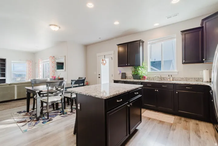 Kitchen island featuring a granite-style countertop, dark cabinetry, and wood-finish flooring