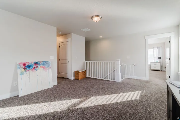 Carpeted upper-level landing with white railing, light gray wall tones, and recessed lighting