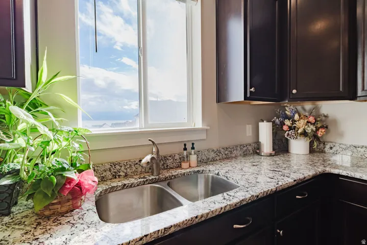 Kitchen sink area featuring a dual basin stainless steel sink with a high-arc faucet, granite countertops, and dark wood cabinetry