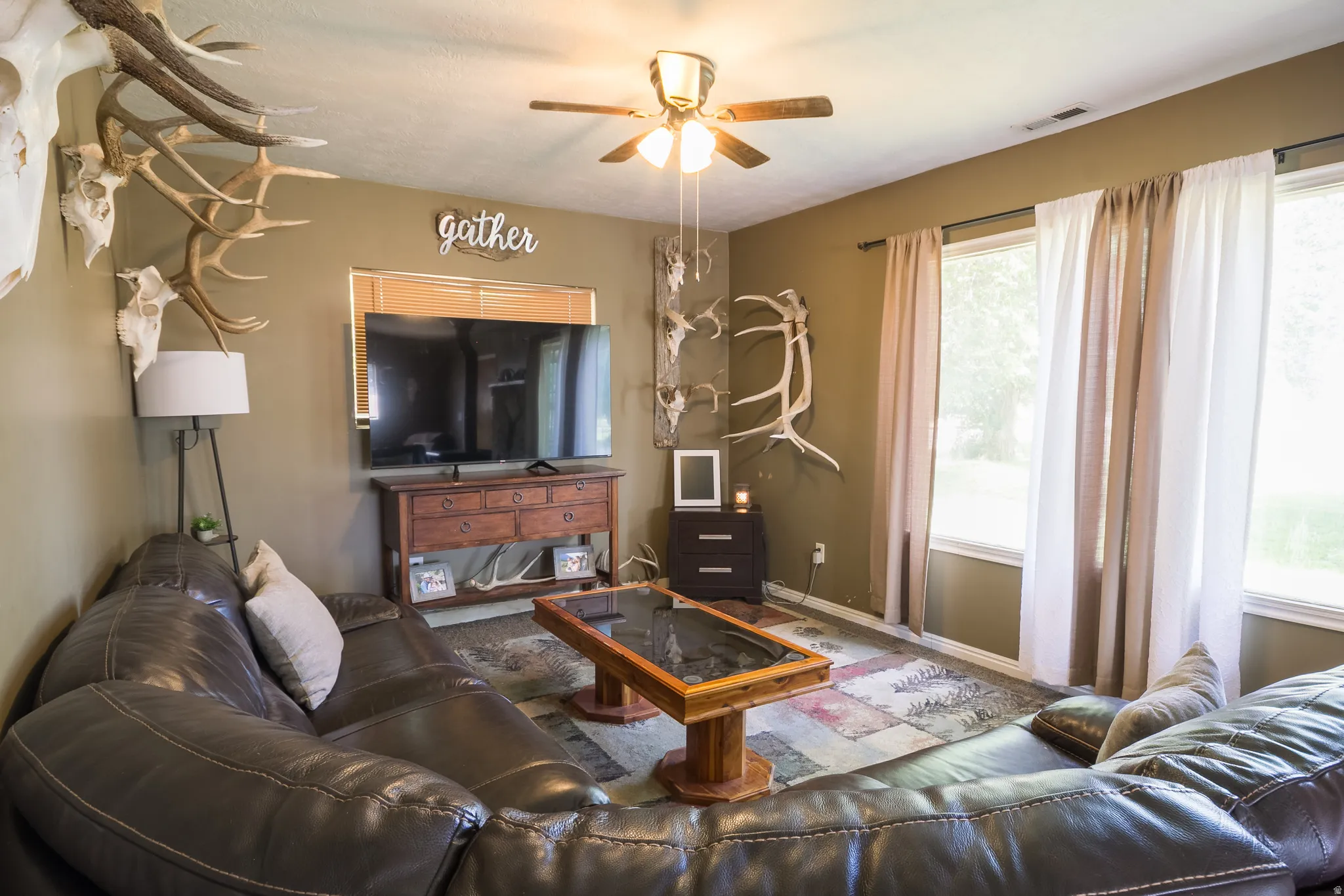 Living area featuring multiple windows, a ceiling fan with integrated lighting, and a wood-finish entertainment console