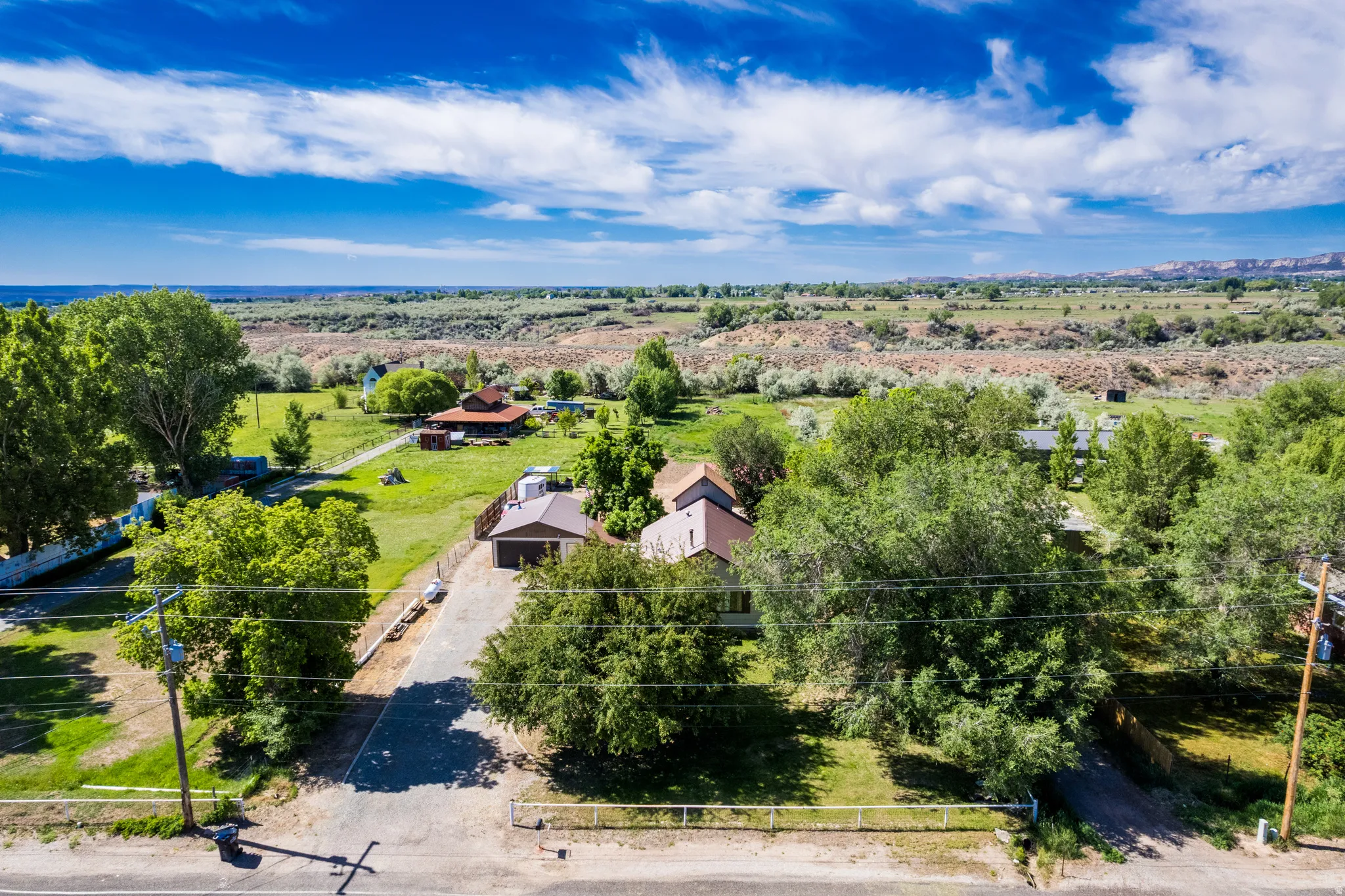 Expansive property featuring multiple structures, mature trees, a gravel driveway, and a broad natural landscape beyond