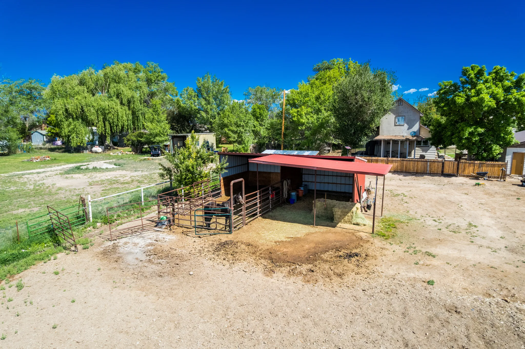 Barn structure with a red metal roof, fenced animal enclosures, and an open dirt area