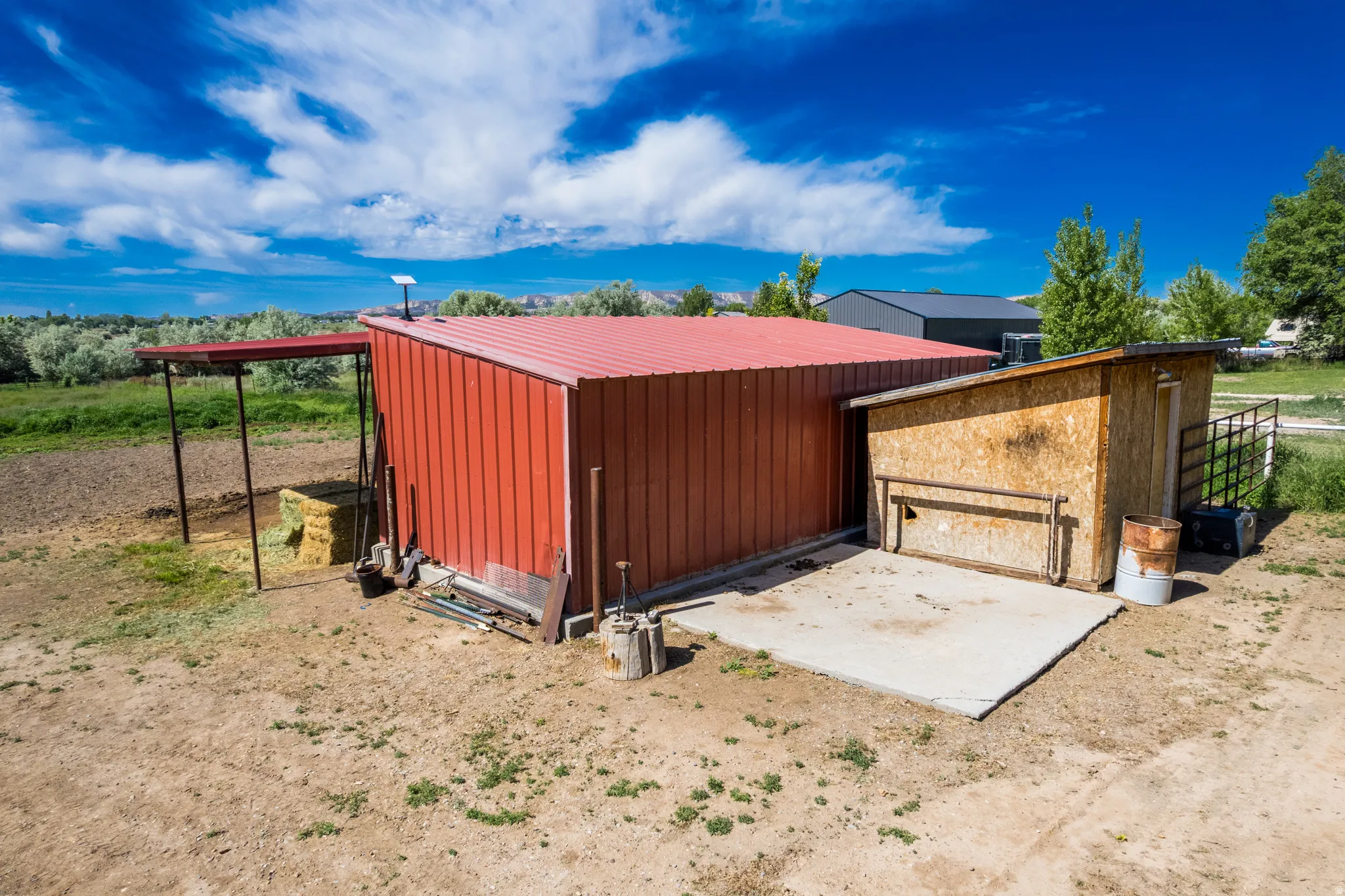 Red metal utility building featuring a concrete pad and a wood-sided lean-to structure