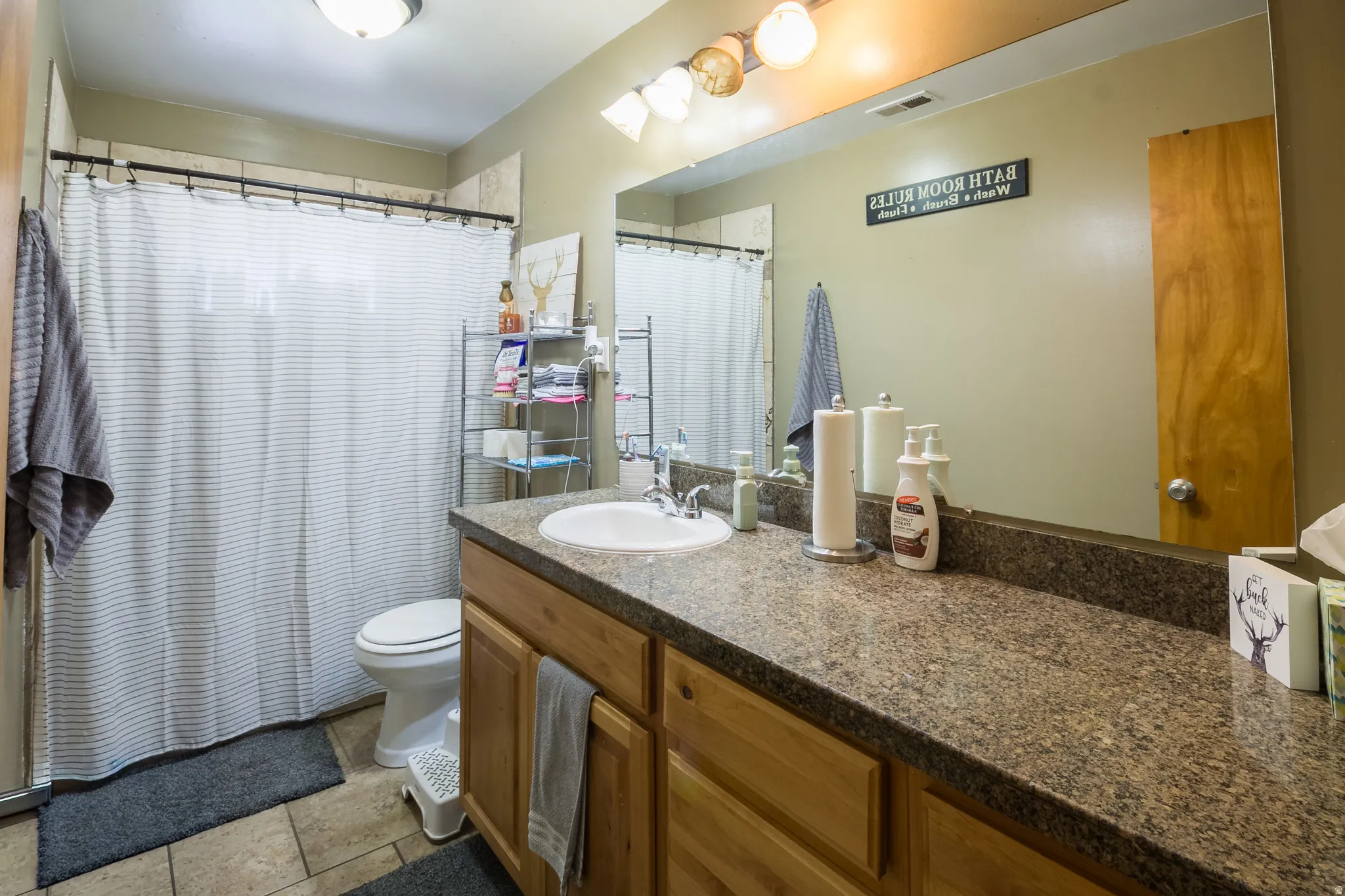 Bathroom vanity featuring a single basin sink, speckled countertop, and light wood-finish cabinetry