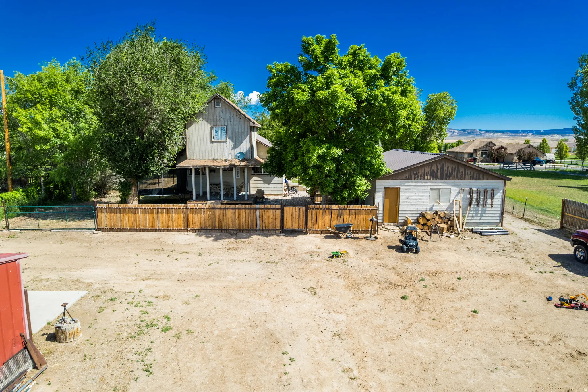 Expansive outdoor area featuring a two-story residence with a covered front porch, a separate utility building with a metal roof, and a wood-slat privacy fence