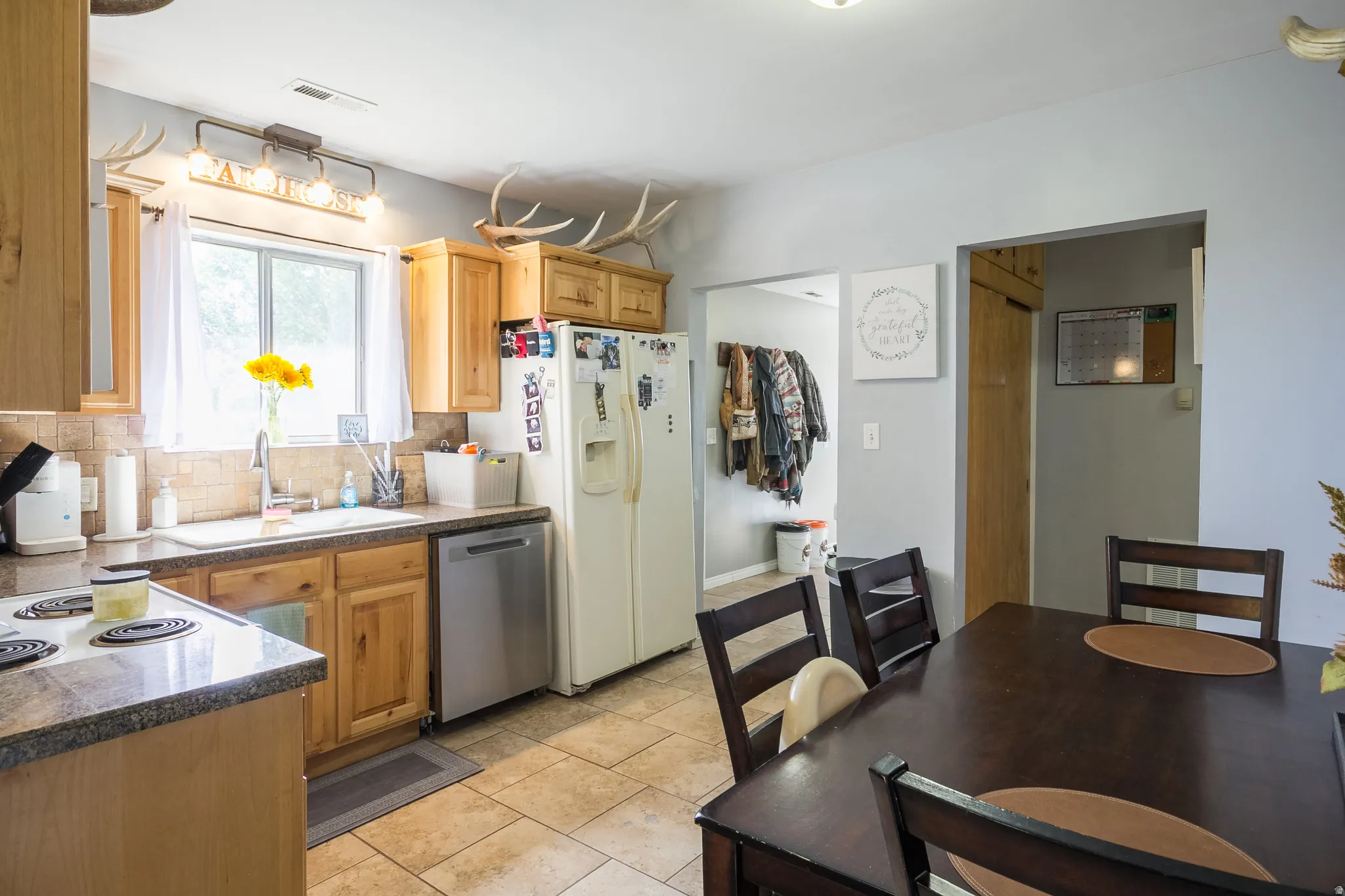 Kitchen and dining area featuring wood-finish cabinetry, a large window above the sink, a stainless steel dishwasher, and a refrigerator