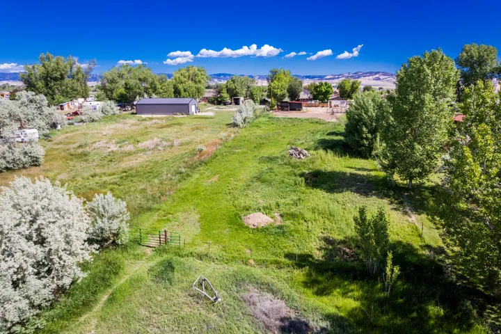 Expansive property featuring a large green field, mature trees, a river, and a dark-colored storage building with white trim