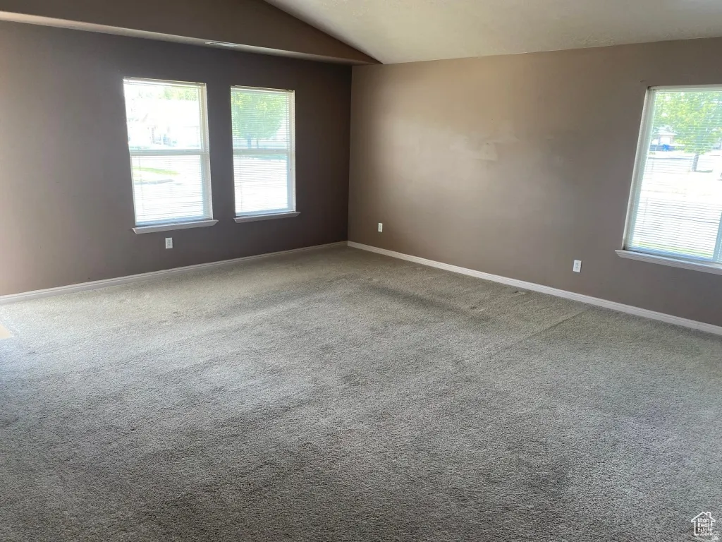 Spacious living room featuring vaulted ceilings, light brown carpeting, and multiple windows with white trim