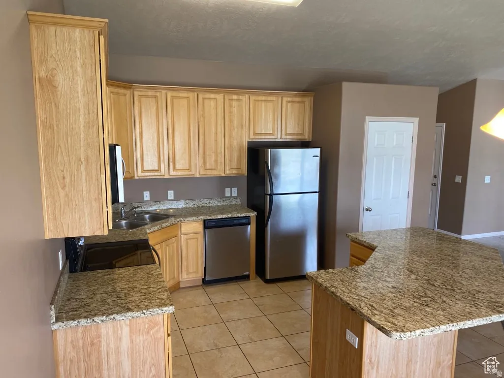 Kitchen featuring light wood cabinetry, granite countertops, tile flooring, and stainless steel appliances including a refrigerator and dishwasher
