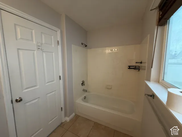 Tub/shower combination with a single-handle fixture, tiled flooring, and a window with a sill