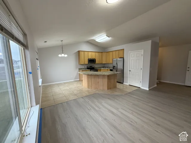 Kitchen featuring wood-finish cabinetry, stainless steel appliances, and a granite island vaulted ceiling.