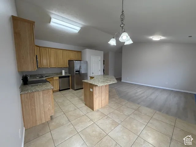 Kitchen featuring wood-finish cabinetry, stainless steel appliances, granite countertops, vaulted ceiling, and a center island with a breakfast bar