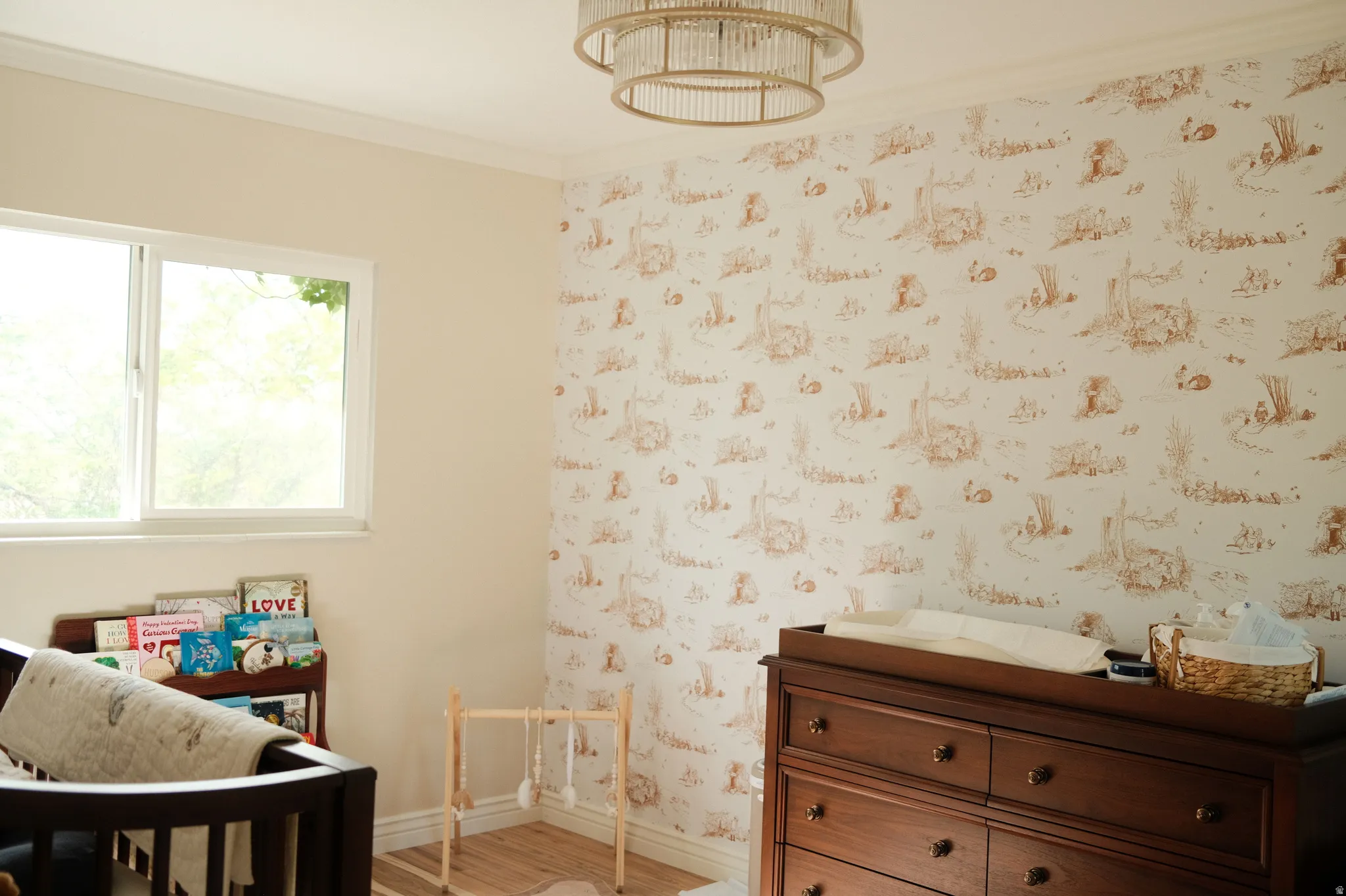 Spacious room featuring a large window, a decorative wallpaper accent wall, wood-finish flooring, and crown molding