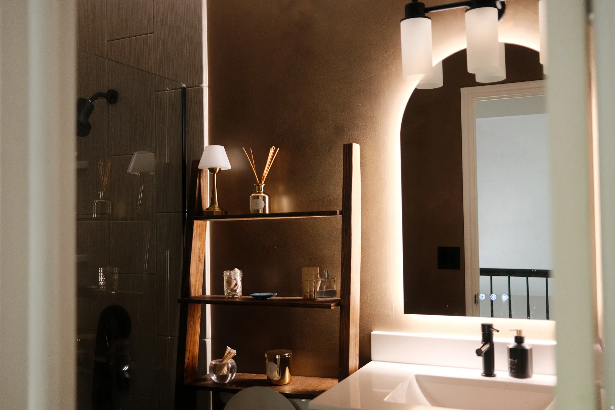 Contemporary bathroom featuring a back-lit arched mirror, white integrated sink, and a matte black faucet