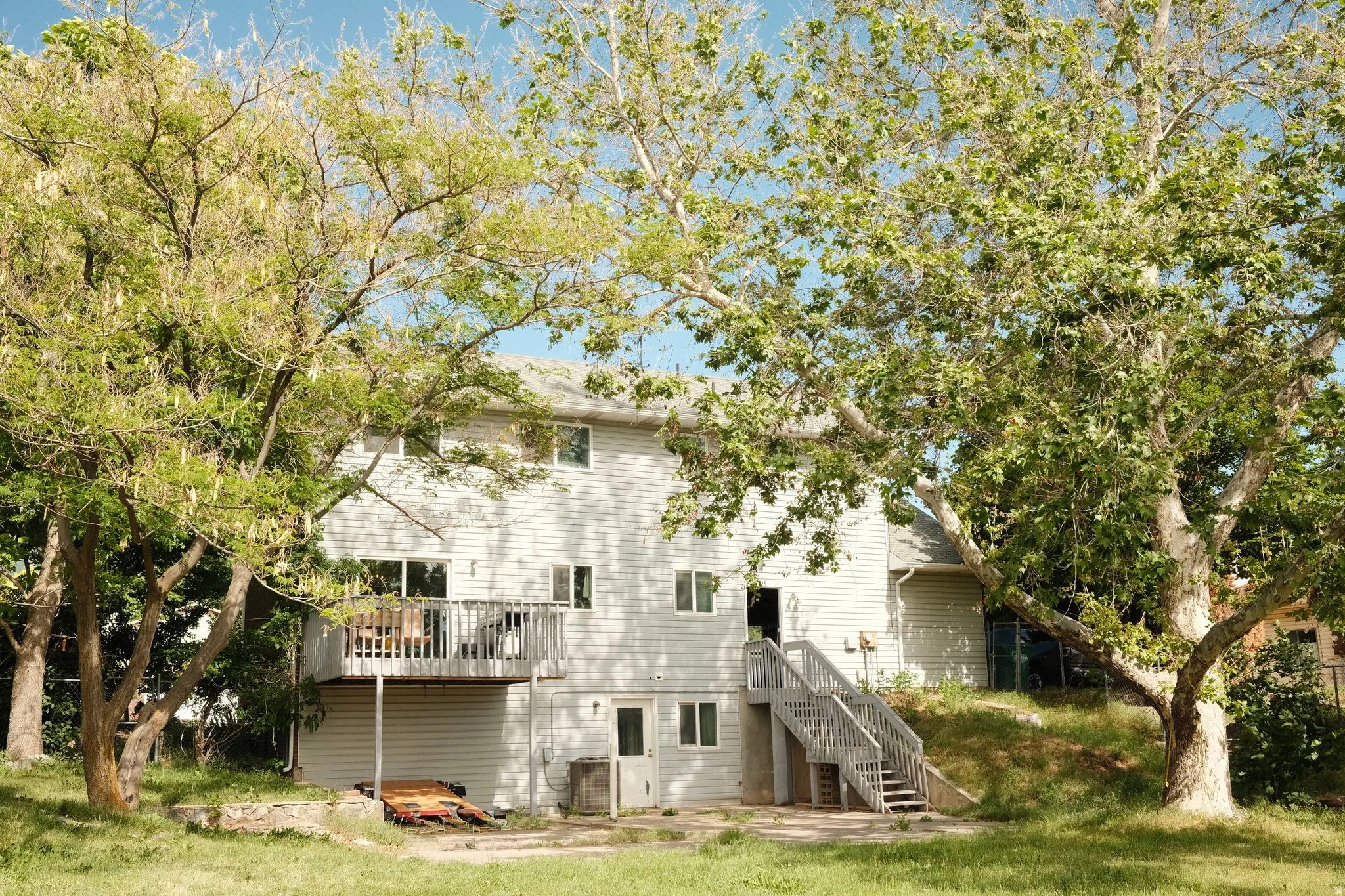 Rear exterior featuring a second-story deck with sliding glass door access, ground-level patio, and exterior stairs