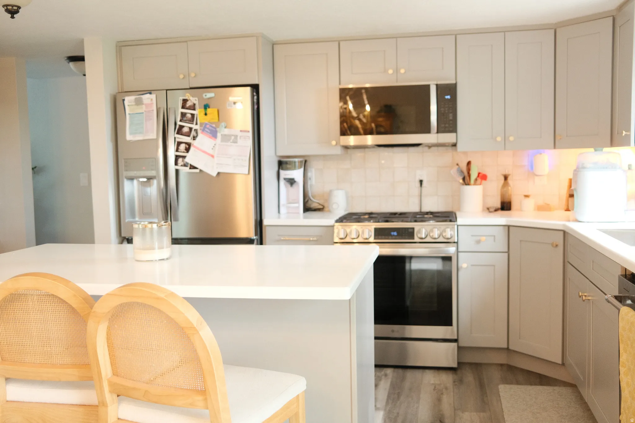 Contemporary kitchen featuring a spacious island with a solid surface countertop, light gray cabinetry, stainless steel appliances, a tiled backsplash, and wood-finish flooring