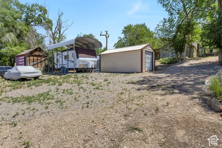 Gravel driveway with multiple outbuildings, including a metal storage shed and an open-sided carport