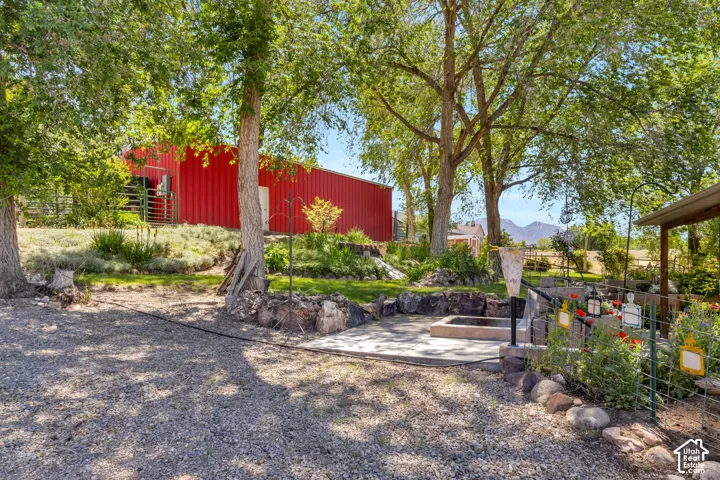 Spacious outdoor area featuring a gravel path, mature trees, and a concrete patio with a built-in fire pit