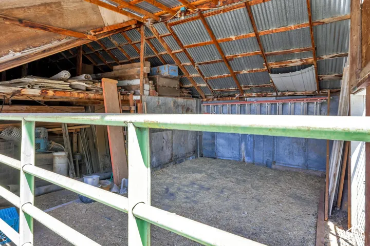 Agricultural structure featuring a corrugated metal roof, exposed wood beam framing, and concrete walls