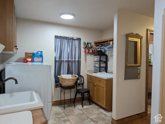 Dedicated laundry space featuring a utility sink, integrated cabinetry with wood-finish doors, a window, and tile flooring