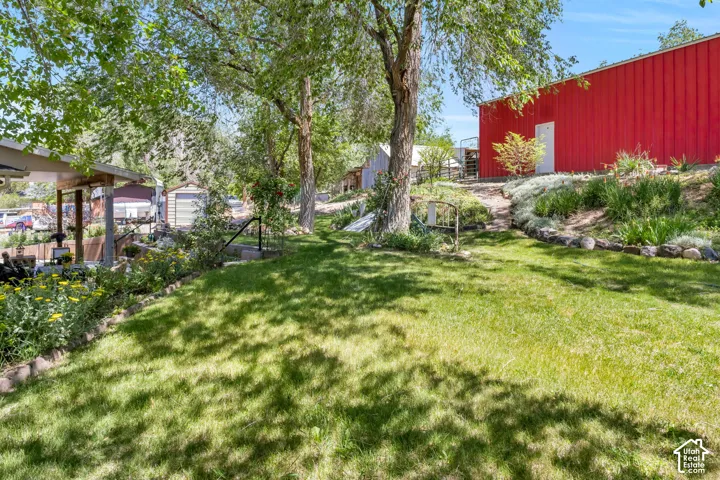 Expansive backyard featuring a manicured lawn, established trees providing shade, and a tiered rock garden with plantings