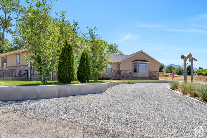 Gravel driveway leading to a residence featuring a tan stucco exterior with stone accents