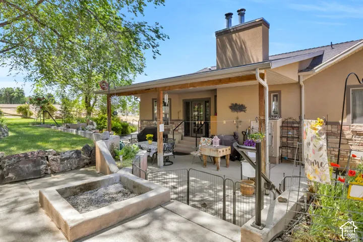 Rear exterior featuring a covered patio with exposed beam accents, stucco and stone facade, concrete patio, built-in fire pit, and a grassy yard with mature trees