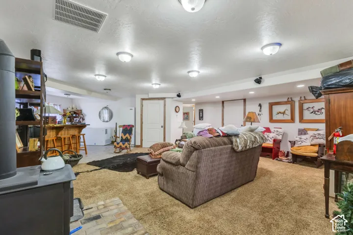 Finished basement space featuring carpeted and tiled flooring, a built-in wet bar, a wood-burning stove with brick hearth, and multiple flush-mount ceiling lights