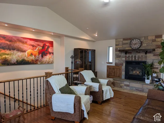 Spacious living area featuring a stone-clad fireplace with wood mantel, vaulted ceilings, recessed lighting, wood-finish flooring, and a wrought iron and wood staircase railing