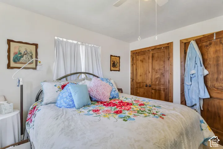 Bedroom featuring a ceiling fan, window with white curtains, and wood-finish closet doors