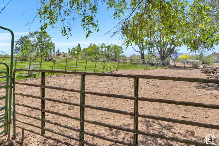 Expansive outdoor area featuring a metal fence and gate, a large field with green foliage, and mature trees
