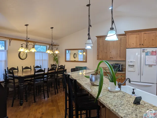 Open-concept kitchen and dining area featuring wood-finish flooring, vaulted ceilings, and a kitchen island with granite-style countertops