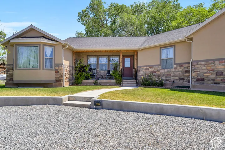 Front elevation featuring a curved concrete walkway, a covered porch with a dark red entry door, a bay window, and a gravel driveway