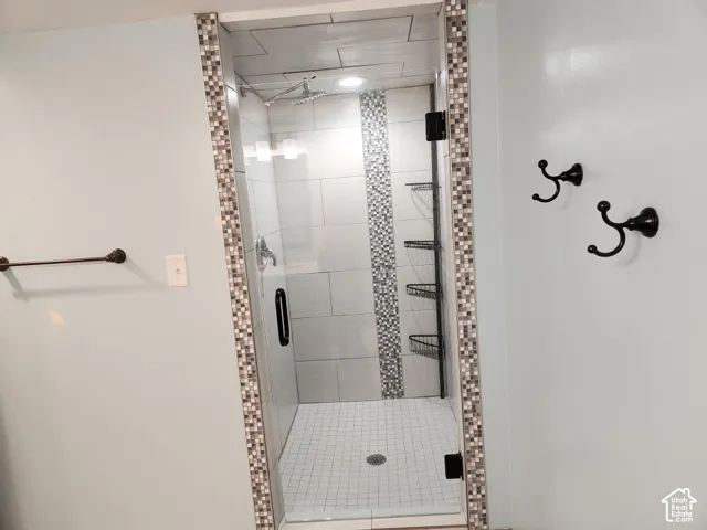 Glass-enclosed shower featuring a mosaic tile accent strip, rainfall showerhead, and built-in shelving