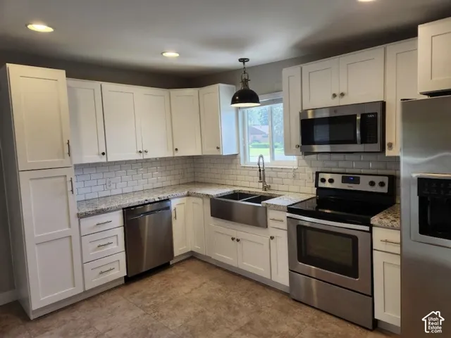 Modern kitchen featuring white shaker cabinetry, stainless steel appliances, speckled stone countertops, a subway tile backsplash, and wood-finish flooring