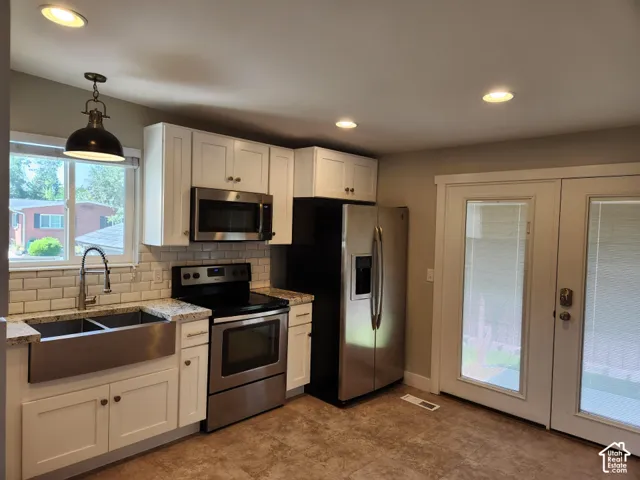 Kitchen featuring white cabinetry, stainless steel appliances, a farmhouse sink, subway tile backsplash, and light-toned flooring