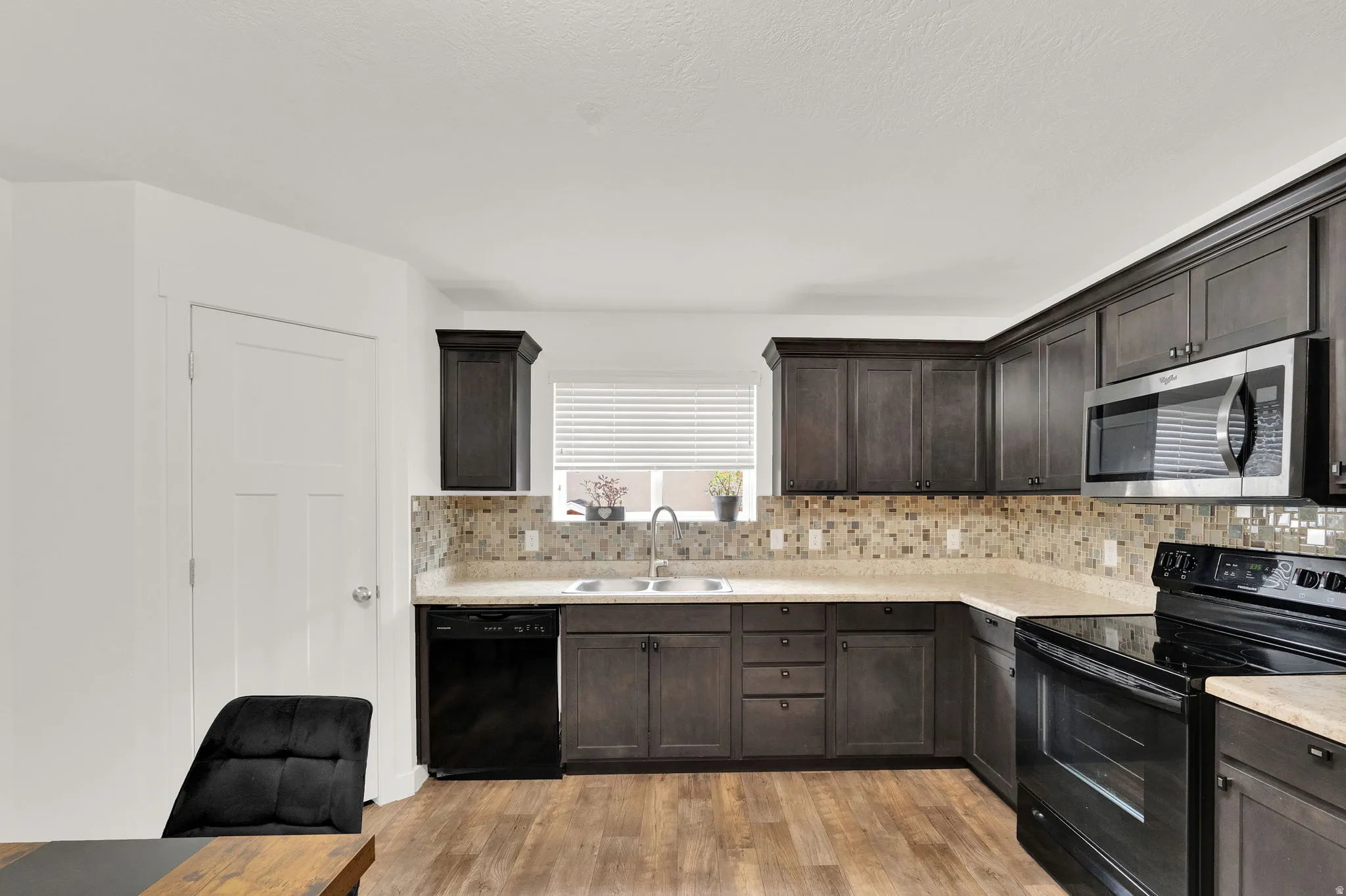 Kitchen featuring dark wood cabinetry, light-toned countertops, and a mosaic tile backsplash