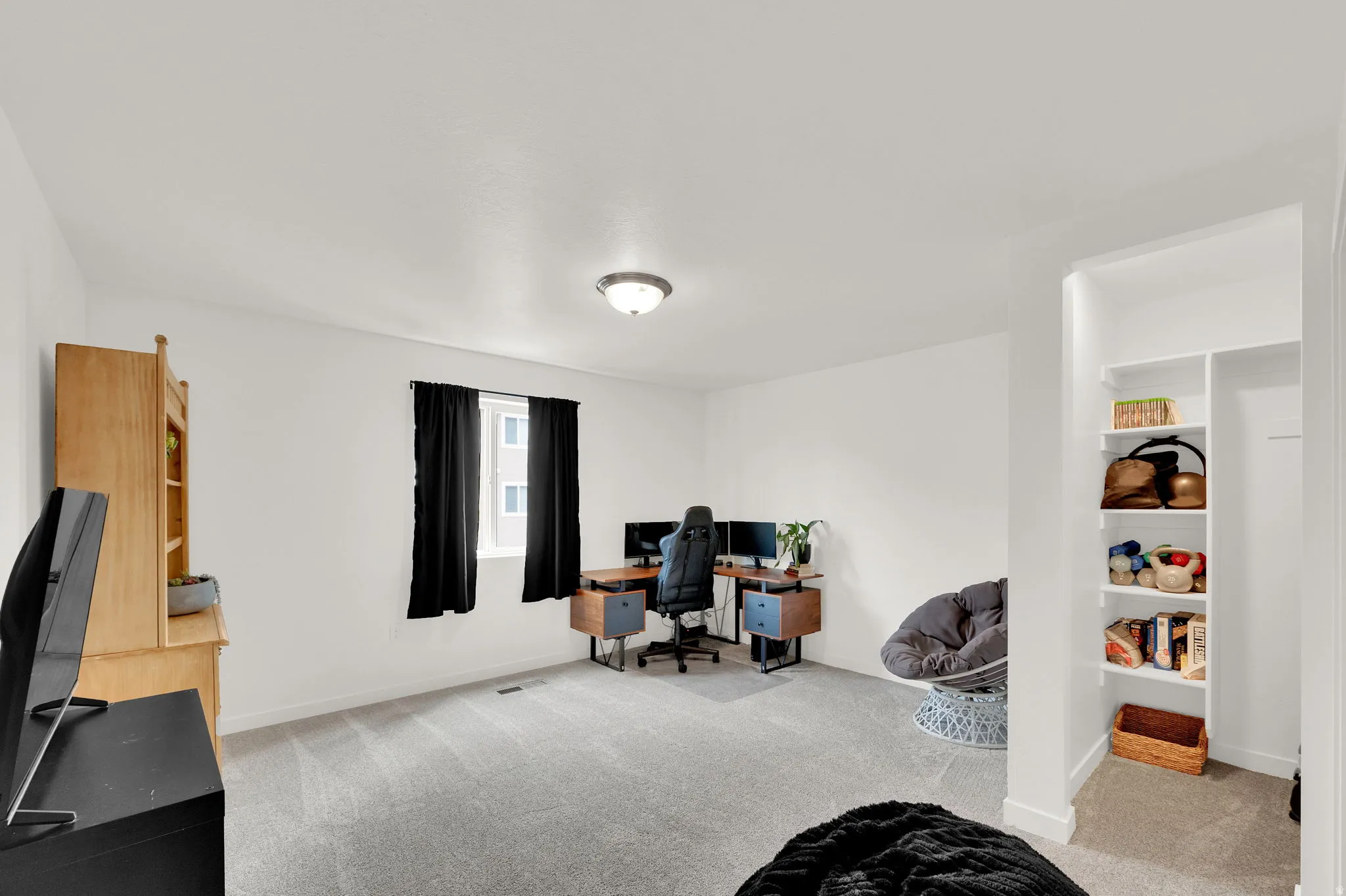 Carpeted interior space featuring a window with black curtains, a built-in recessed shelving unit, and a ceiling-mounted light fixture